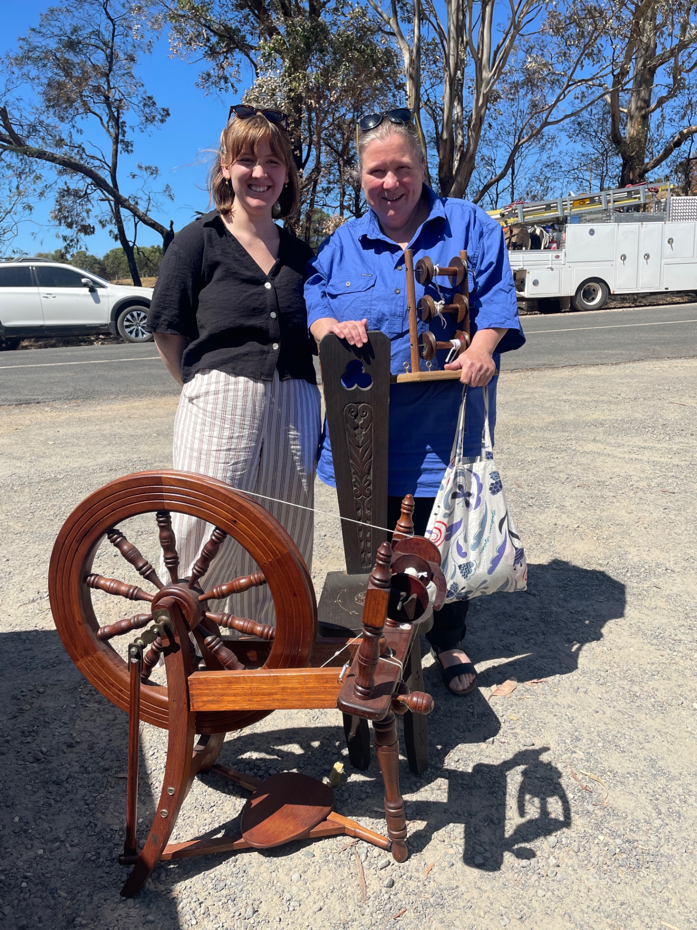 Two women smiling beside a donated spinning wheel on a country roadside
