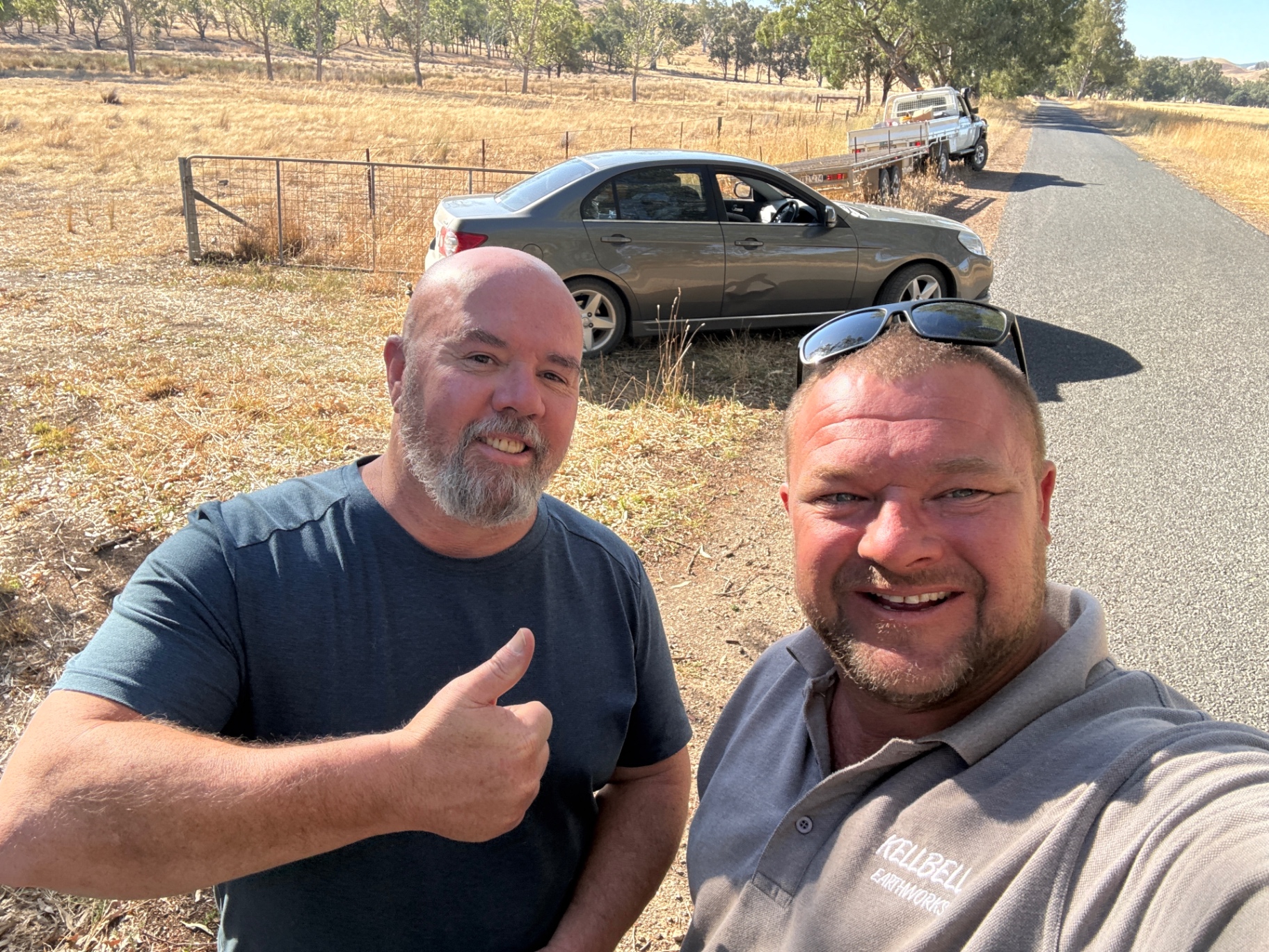 Two volunteers smiling beside a car and trailer on a country road
