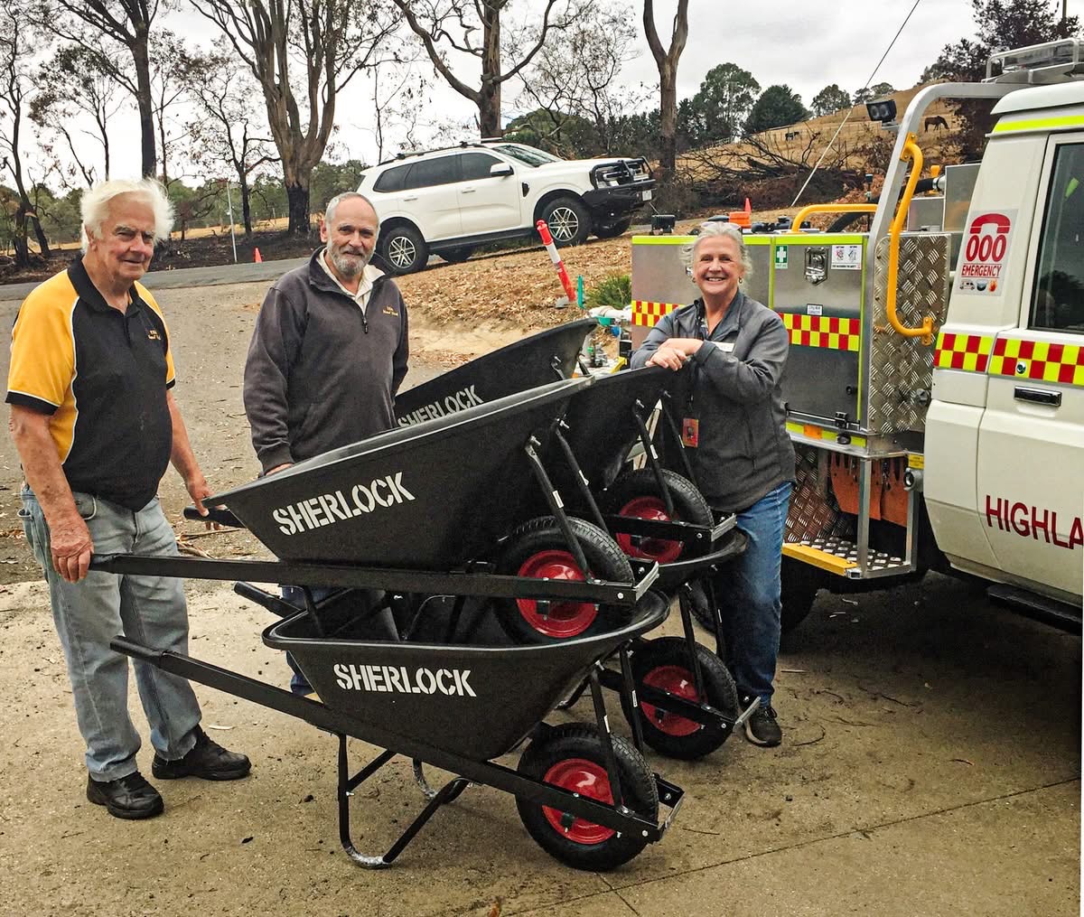 Three community members with donated wheelbarrows beside the Highlands fire truck