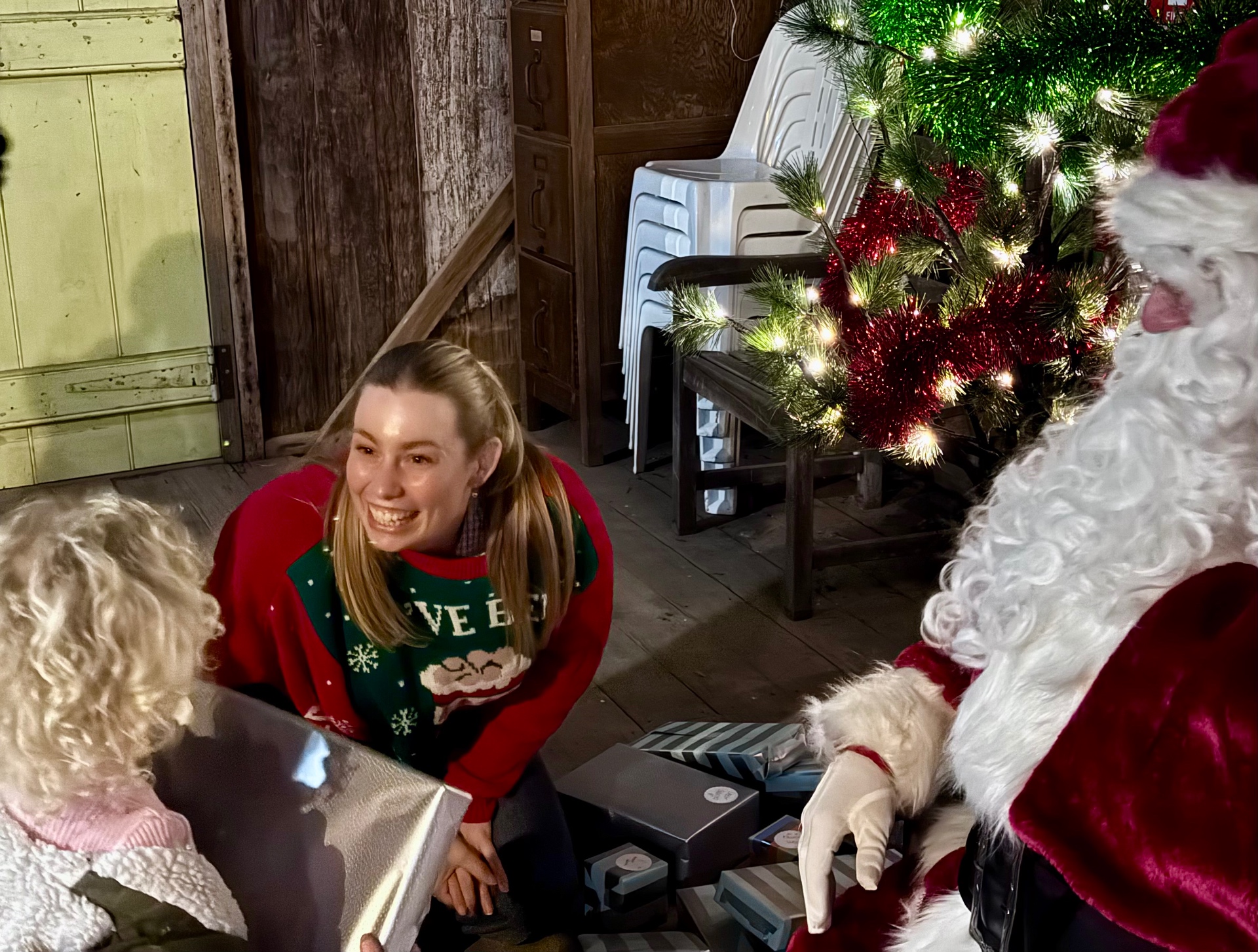 A volunteer in a Christmas jumper handing presents to Santa