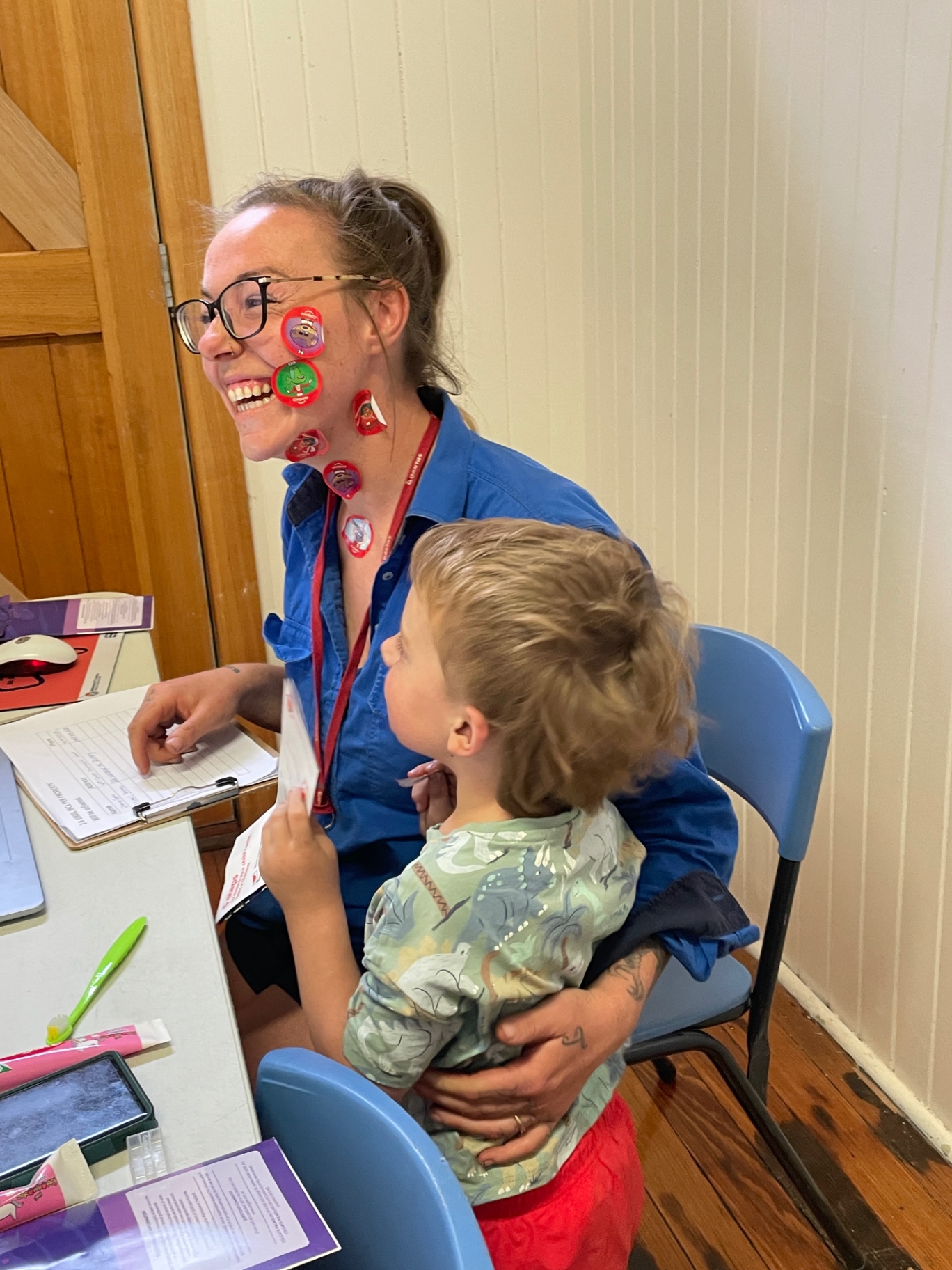 A health worker covered in stickers with a young child on her lap at the hall