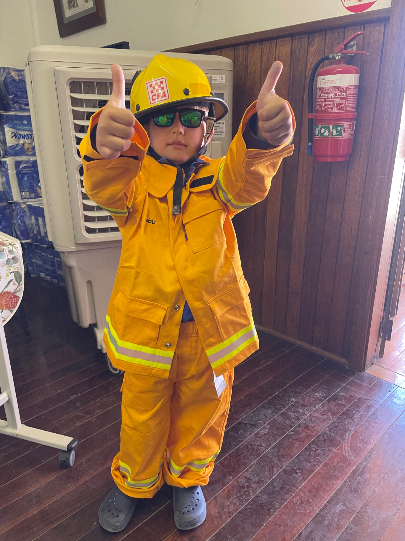 A young child dressed in CFA turnout gear giving two thumbs up