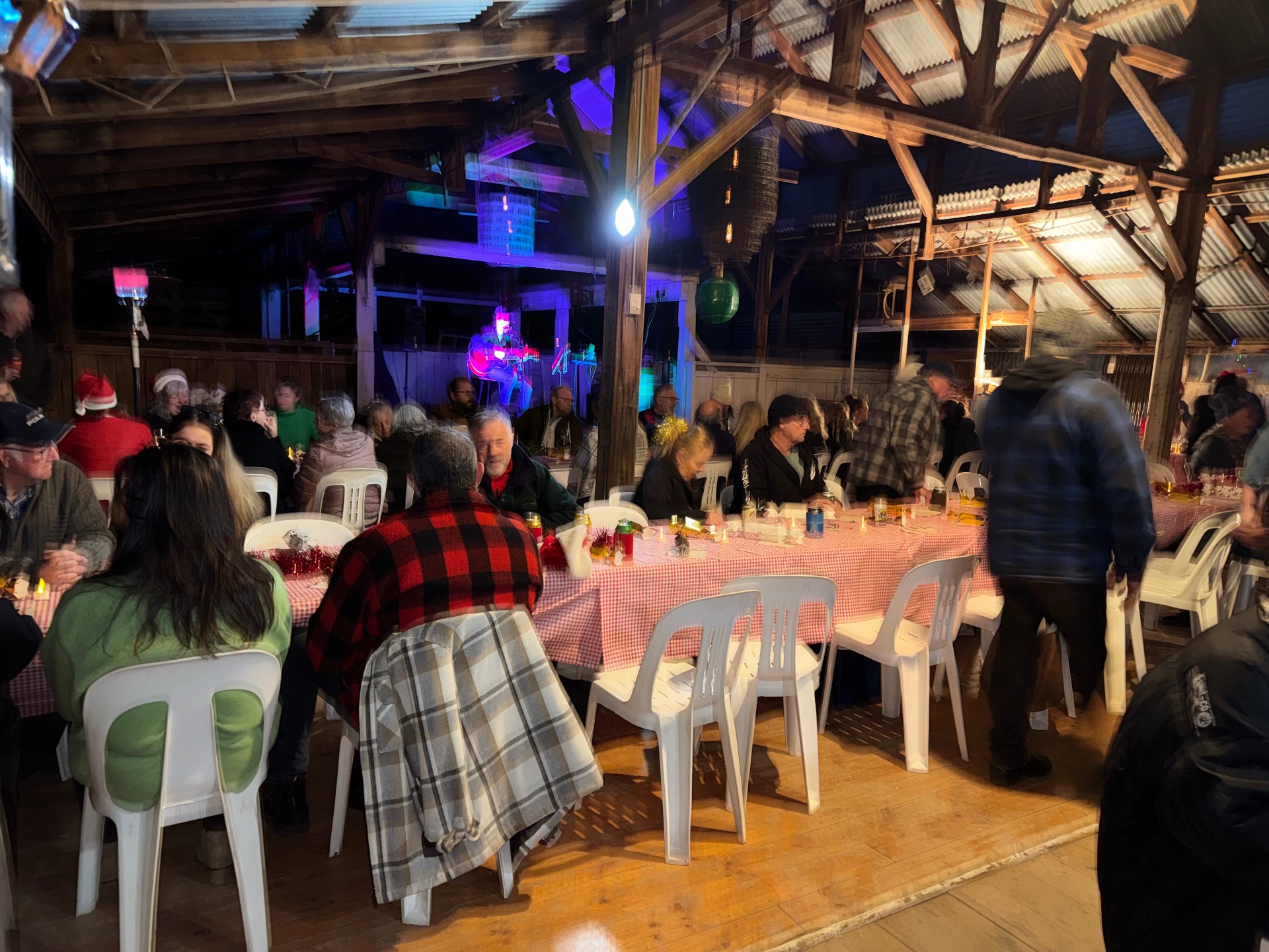 A crowd at long tables with a guitarist playing on stage