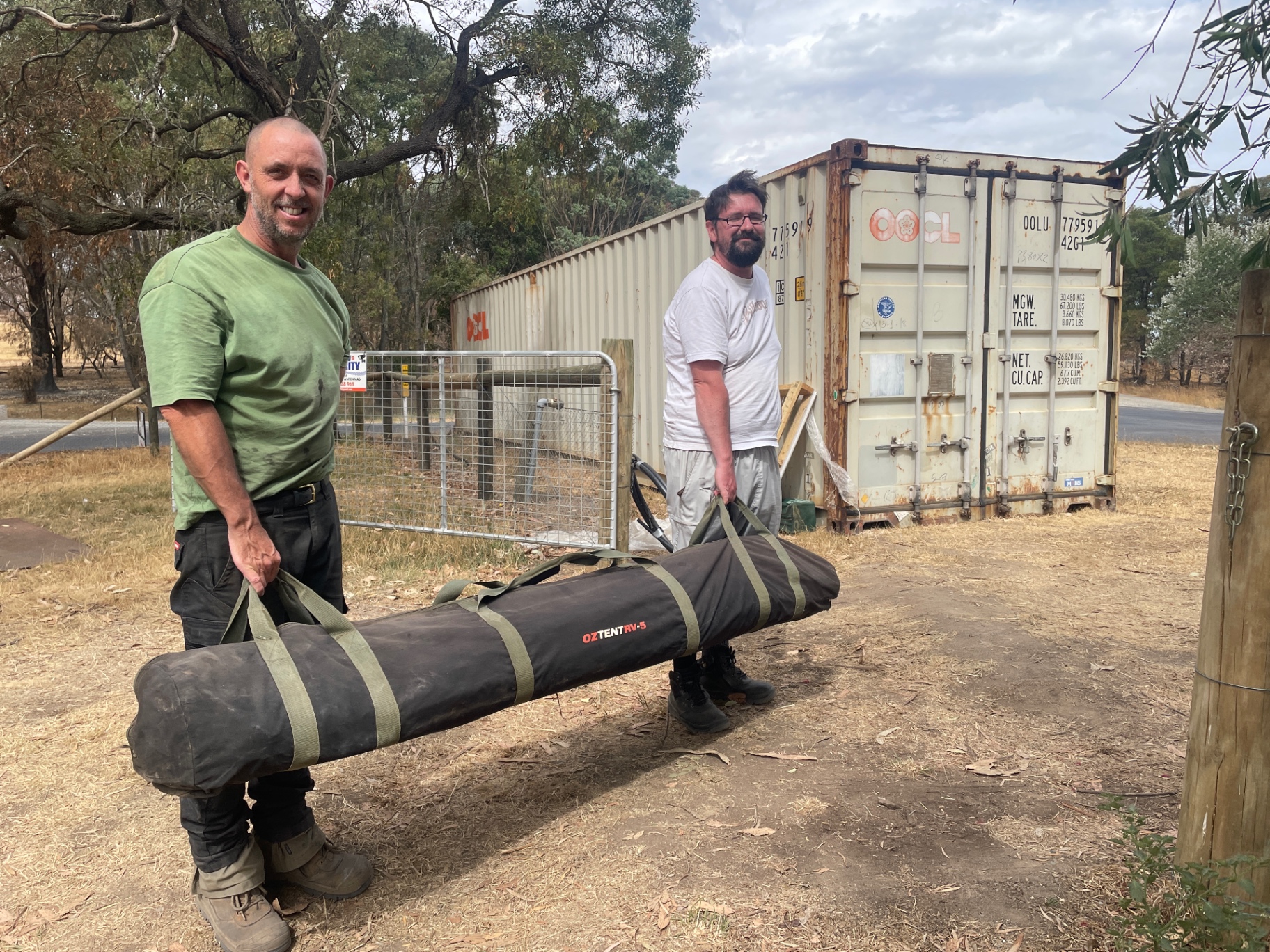 Two volunteers carrying a donated tent from the supply containers