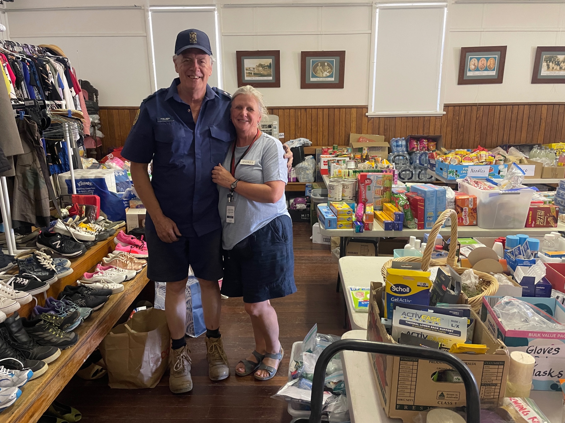 Two volunteers standing among donated clothing, food and supplies inside the hall
