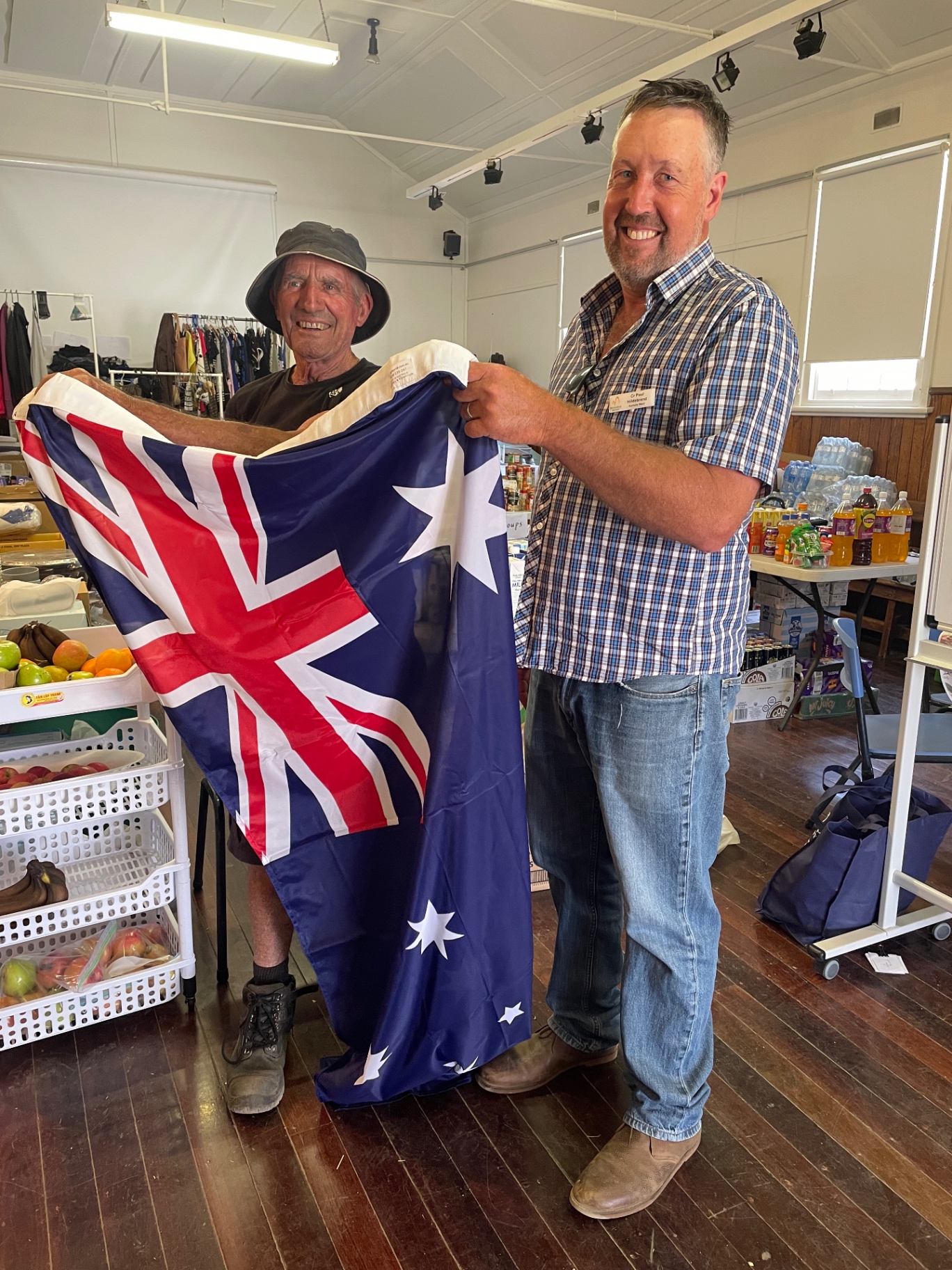 Two men holding up an Australian flag inside the hall surrounded by donated supplies