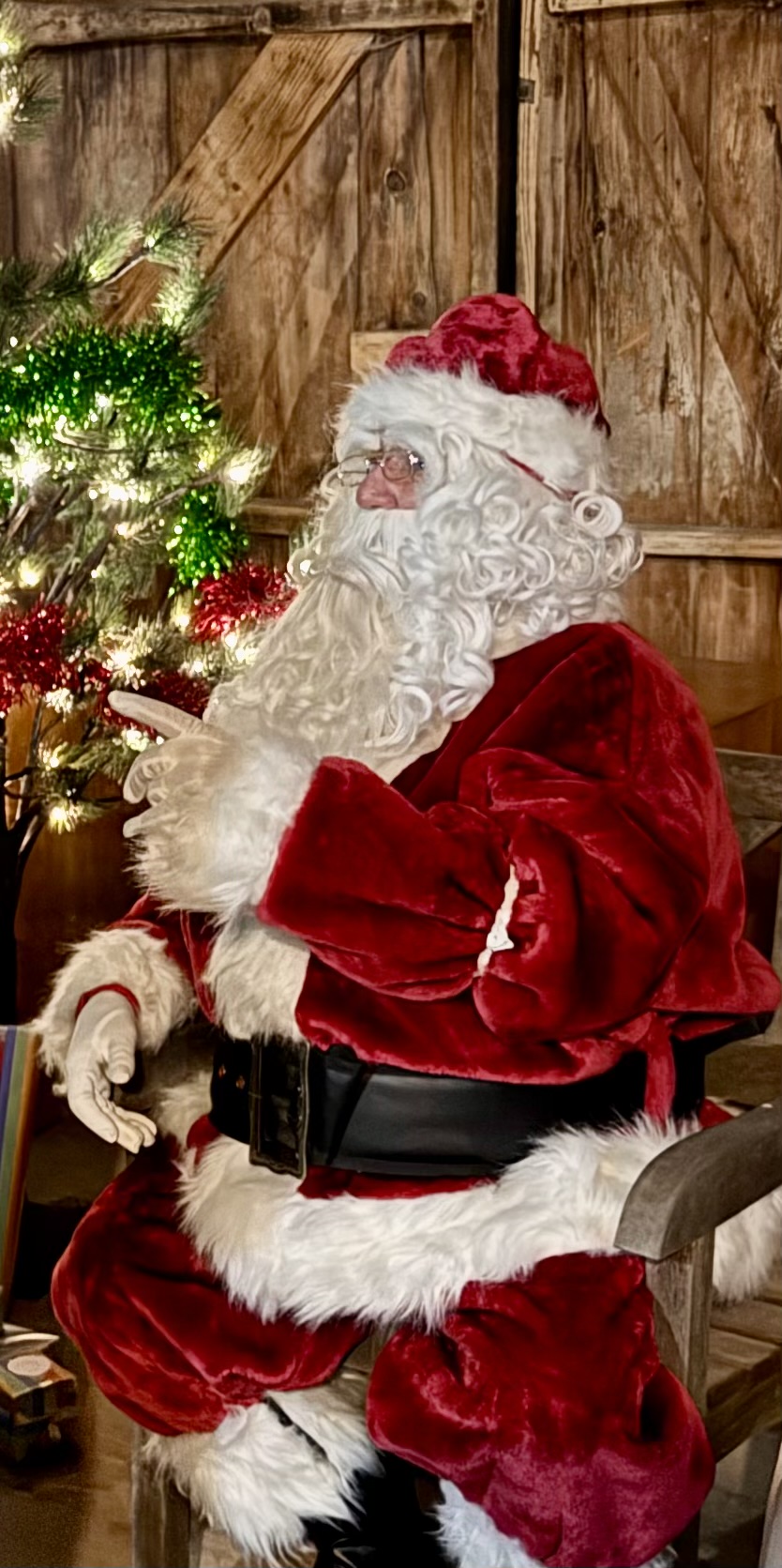 Santa seated beside a lit Christmas tree with his sack of presents